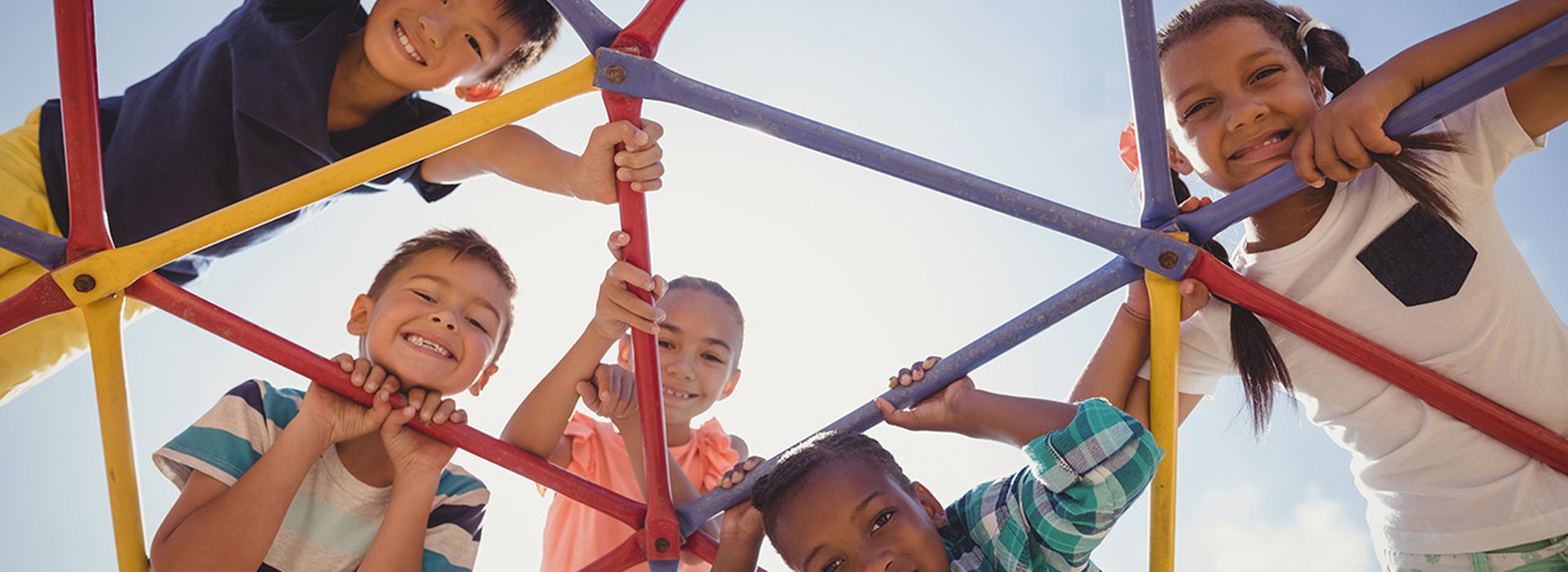 Portrait-of-happy-schoolkids-looking-through-dome-climber